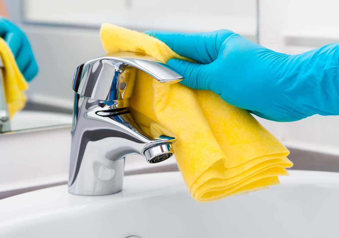 Gloved hand polishing stainless steel sink faucet